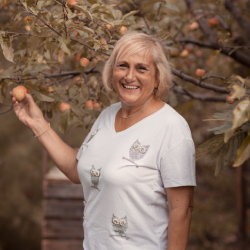 Natural Pharmaceuticals FlexiMed® Active Idős nő rózsaszín sportpulóverben kerékpározik napsütéses parkban, egészséges életmódot élve.